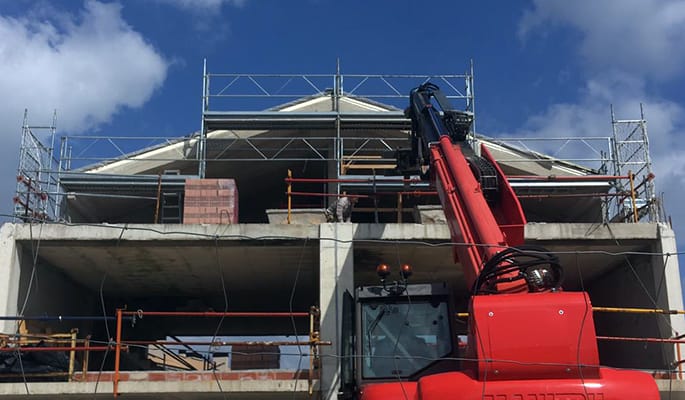 Foto tomada frente a la vivienda que muestra el progreso en las obras, con andamios y una grúa elevadora.